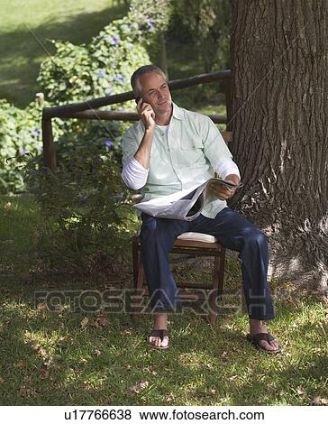 Stock Photo - Man talking on a mobile phone, sitting next to a tree. Fotosearch