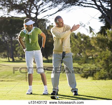 Stock Image - Man teaching a woman how to play golf. Fotosearch