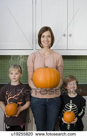 Mother and two children in the kitchen holding orange Hallowe'en pumpkins View Large Photo Image Stock Image - Mother and two children in the kitchen holding orange Hallowe'en pumpkins. Fotosearch