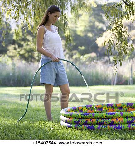 Picture - Mother filling a paddling pool with a garden hose. Fotosearch