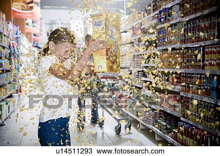 Stock Image - Naughty young girl emptying cereal packet in a supermarket. Fotosearch