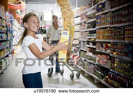 Stock Image - Naughty young girl emptying cereal packet in a supermarket. Fotosearch