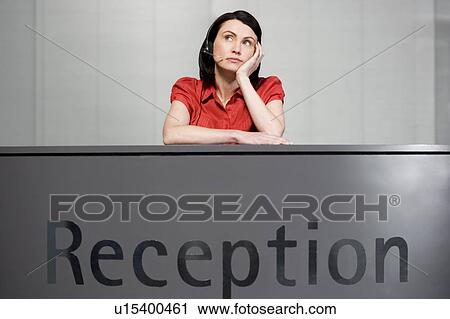 Stock Image - Office receptionist in a red blouse, looking bored. Fotosearch