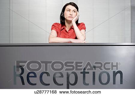 Stock Photo - Office receptionist in a red blouse, looking bored. Fotosearch