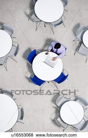 Stock Photo - Overhead view of businessman at table of staff canteen, typing on a laptop. Fotosearch