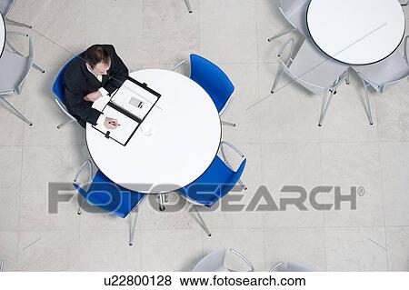 Stock Photo - Overhead view of businessman at table of staff canteen, looking through business papers. Fotosearch