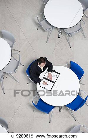 Stock Photography - Overhead view of businessman at table of staff canteen, looking through business papers. Fotosearch