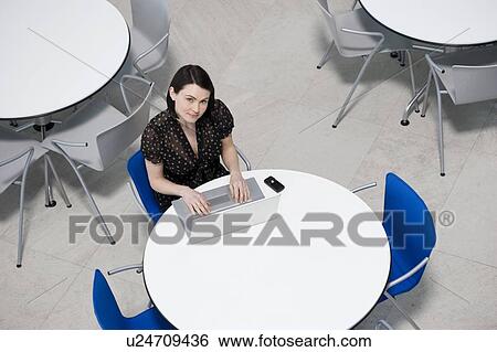 Stock Photograph - Overhead view of businesswoman at table of staff canteen, typing on a laptop. Fotosearch
