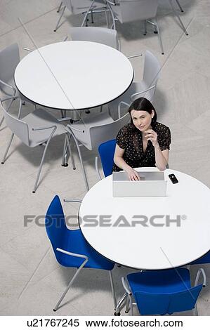 Stock Photography - Overhead view of businesswoman at table of staff canteen, typing on a laptop. Fotosearch