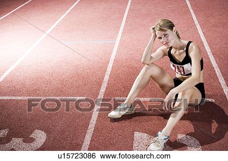 Stock Photograph - Portrait of a female athlete resting and sitting on the running track. Fotosearch