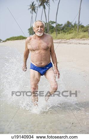 Picture - Portrait of a senior man in swimming trunks at the beach . Fotosearch