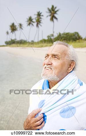 Stock Image - Portrait of a senior man wrapped in a towel at the beach . Fotosearch