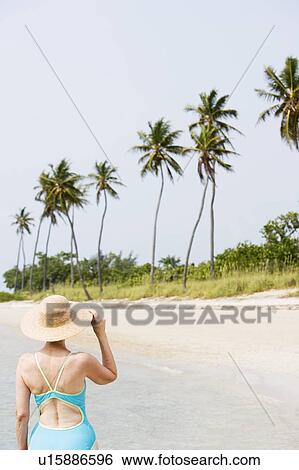 Stock Photograph - Portrait of a senior woman in a swimsuit at the beach wearing a straw hat. Fotosearch
