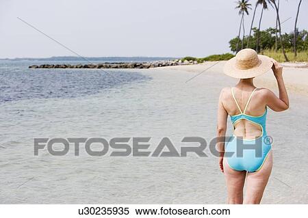 Stock Photography - Portrait of a senior woman in a swimsuit at the beach wearing a straw hat. Fotosearch