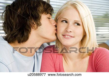 Stock Photo - Portrait of a teenage couple with the boy kissing the girl. Fotosearch
