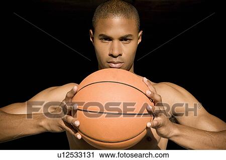 Stock Image - Portrait of a young African American man holding a basketball. . Fotosearch