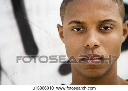 Stock Image - Portrait of a young African American man in front of a graffiti covered wall. Fotosearch