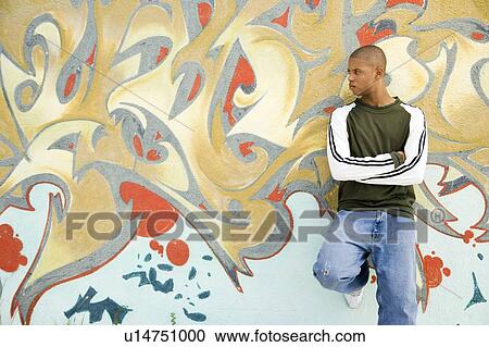 Stock Image - Portrait of a young African American man in front of a graffiti covered wall. Fotosearch