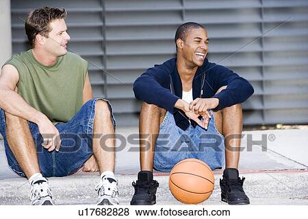 Portrait of a young African American and Caucasian men sitting smiling with a basketball View Large Photo Image Stock Photo - Portrait of a young African American and Caucasian men sitting smiling with a basketball. Fotosearch