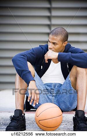 Stock Photograph - Portrait of a young African American man sitting with a basketball. . Fotosearch