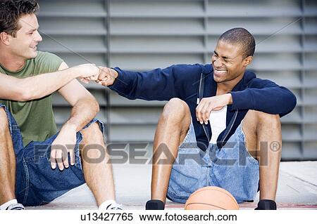 Portrait of a young African American and Caucasian men sitting smiling making greeting hand gestures View Large Photo Image Stock Photography - Portrait of a young African American and Caucasian men sitting smiling making greeting hand gestures . Fotosearch