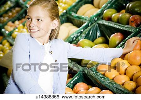 Stock Photograph - Portrait of a young girl holding two grapefruits in a supermarket. Fotosearch