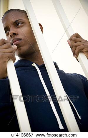 Stock Photo - Portrait of a young man behind bars. Fotosearch