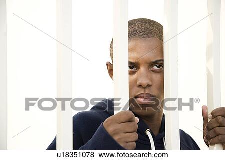 Stock Photo - Portrait of a young man behind bars. Fotosearch