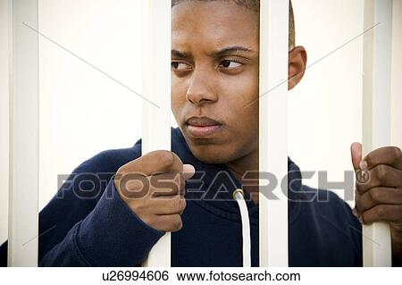 Stock Photograph - Portrait of a young man behind bars. Fotosearch