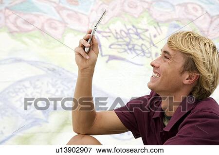 Portrait of a young man on a mobile phone in front of a graffiti covered wall View Large Photo Image Stock Photo - Portrait of a young man on a mobile phone in front of a graffiti covered wall. Fotosearch