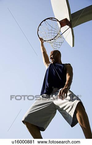 Stock Image - Portrait of young African jumping and hanging from a basketball ring. Fotosearch