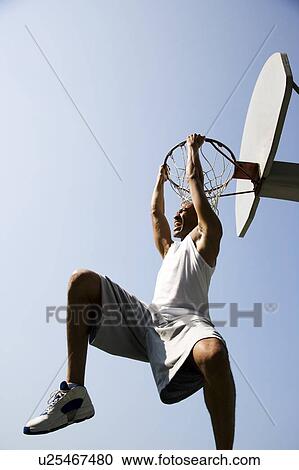Stock Image - Portrait of young African jumping and hanging from a basketball ring. Fotosearch