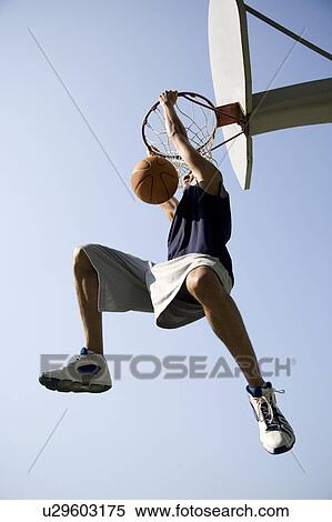 Stock Photography - Portrait of young African jumping and hanging from a basketball ring. Fotosearch