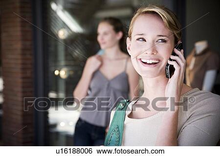Stock Photograph - Portrait of young woman in the street, laughing and chatting on her mobile phone. Fotosearch