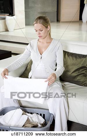 Stock Photo - Pregnant woman folding the washing at home. Fotosearch