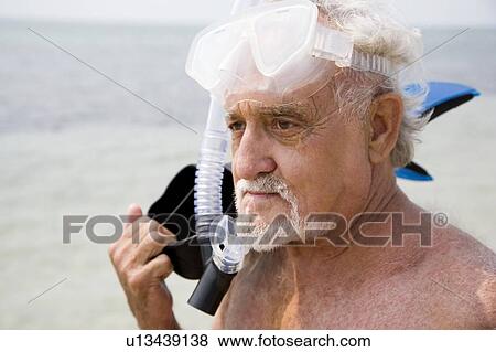 Stock Photo - Senior man with snorkel gear and flippers at the beach . Fotosearch