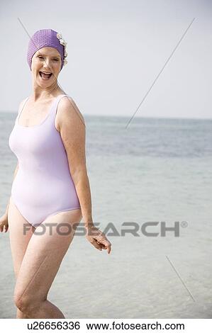Stock Photograph - Senior woman in a swimsuit and swimming hat, at the beach . Fotosearch