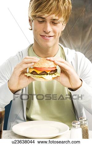Teenage boy eating a large hamburger in a diner View Large Photo Image Picture - Teenage boy eating a large hamburger in a diner . Fotosearch