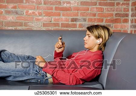 Stock Image - Teenage boy lying on a seat listening to music on mp3. Fotosearch