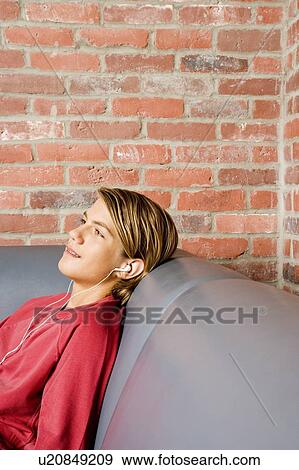 Teenage boy lying on a seat listening to music on mp3 View Large Photo Image Stock Photo - Teenage boy lying on a seat listening to music on mp3. Fotosearch