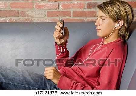 Stock Photography - Teenage boy lying on a seat listening to music on mp3. Fotosearch