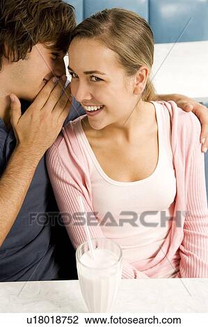 Stock Image - Teenage couple whispering to each other sharing a milkshake sitting in a diner . Fotosearch