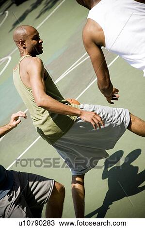Stock Image - Three men playing basketball on an outdoor court . Fotosearch