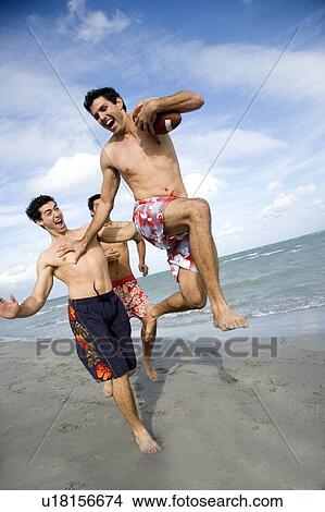 Three young men playing with a ball on a beach View Large Photo Image Picture - Three young men playing with a ball on a beach. Fotosearch