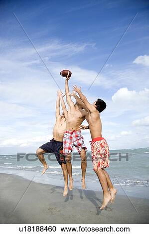 Stock Image - Three young men playing with a ball on a beach. Fotosearch