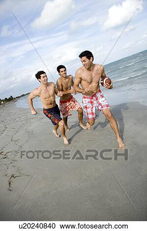 Stock Image - Three young men playing with a ball on a beach. Fotosearch
