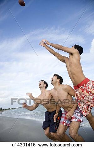 Three young men playing with a ball on a beach View Large Photo Image Stock Photograph - Three young men playing with a ball on a beach. Fotosearch