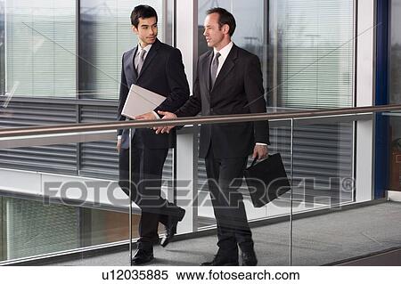 Stock Photography - Two businessmen walking along in modern office building. Fotosearch