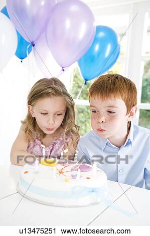 Stock Image - two children blowing out candles on birthday cake. Fotosearch