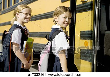 Stock Image - Two schoolgirls getting on a school bus. Fotosearch